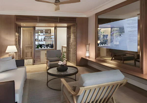 A hotel room featuring a mirror with an integrated TV on the wall, reflecting the room's decor. The space includes a cozy sitting area with a coffee table and wooden furniture.