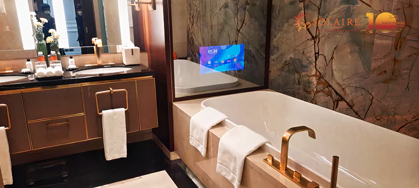 White bathtub in a luxurious restroom with a sophisticated mirror TV and towels.
